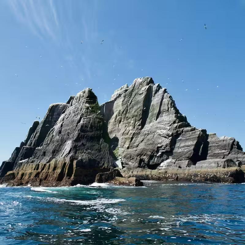 A barren rocky islands juts out of the bright blue ocean.